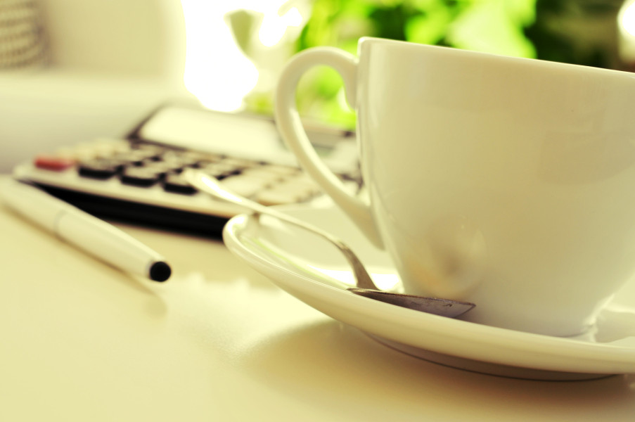 detail of a desk with a calculator and a cup of coffee or tea in an office with a nice atmosphere